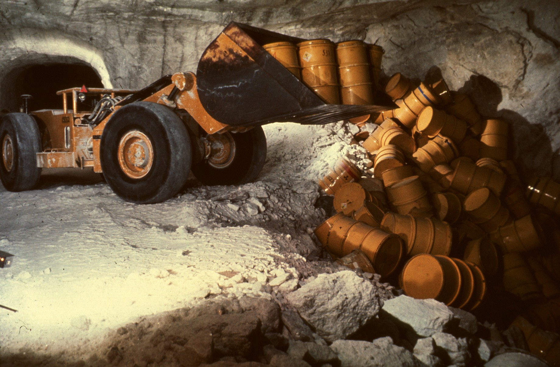 Ein Radlader steht in einem Bergwerksstollen und kippt gelbe Fässer auf den Boden