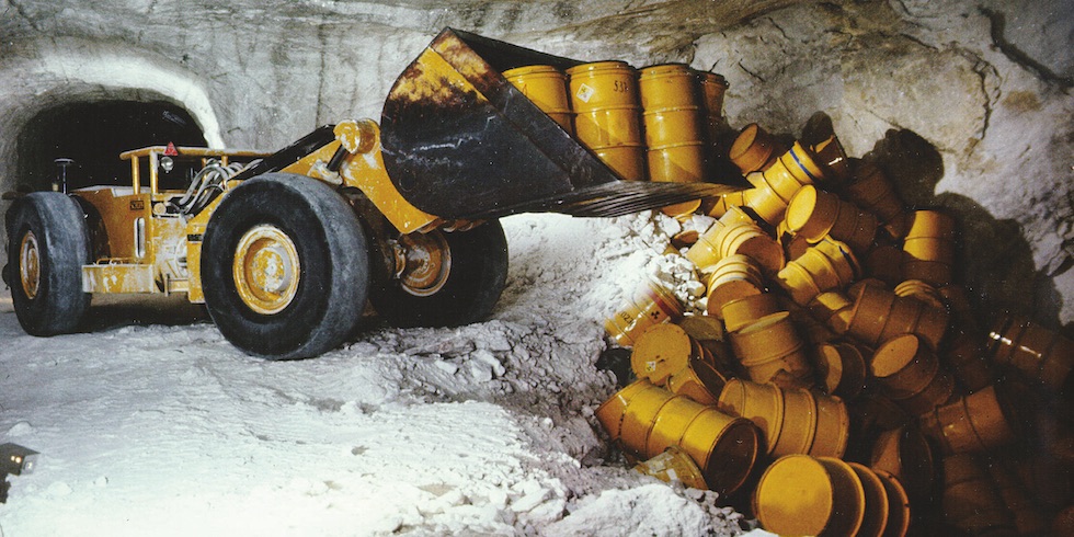 Ein Radlader kippt gelbe Atommüllfässer in ein Loch unter Tage