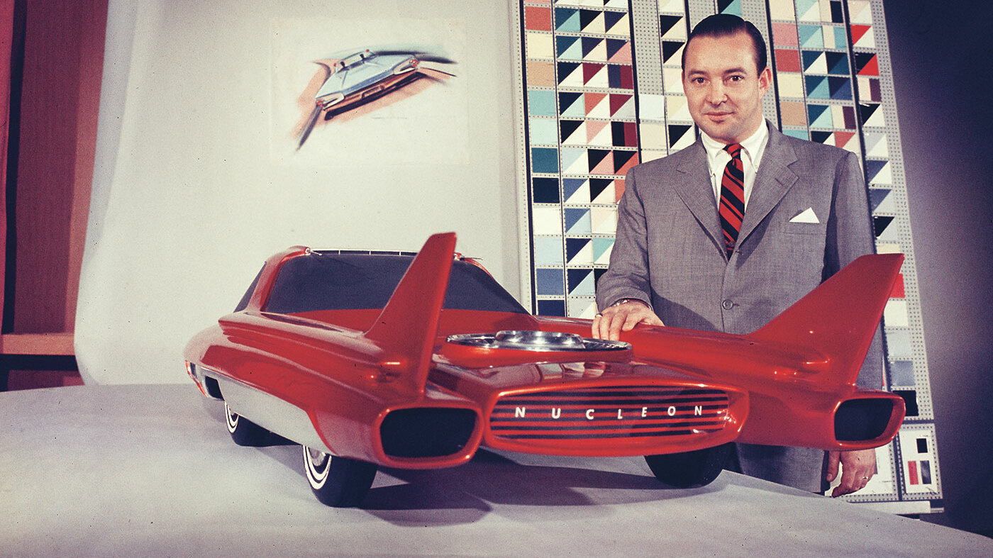Bild aus den 50iger Jahren. Ein Mann im Anzug und Schlips präsentiert stolz ein rotes Automodell