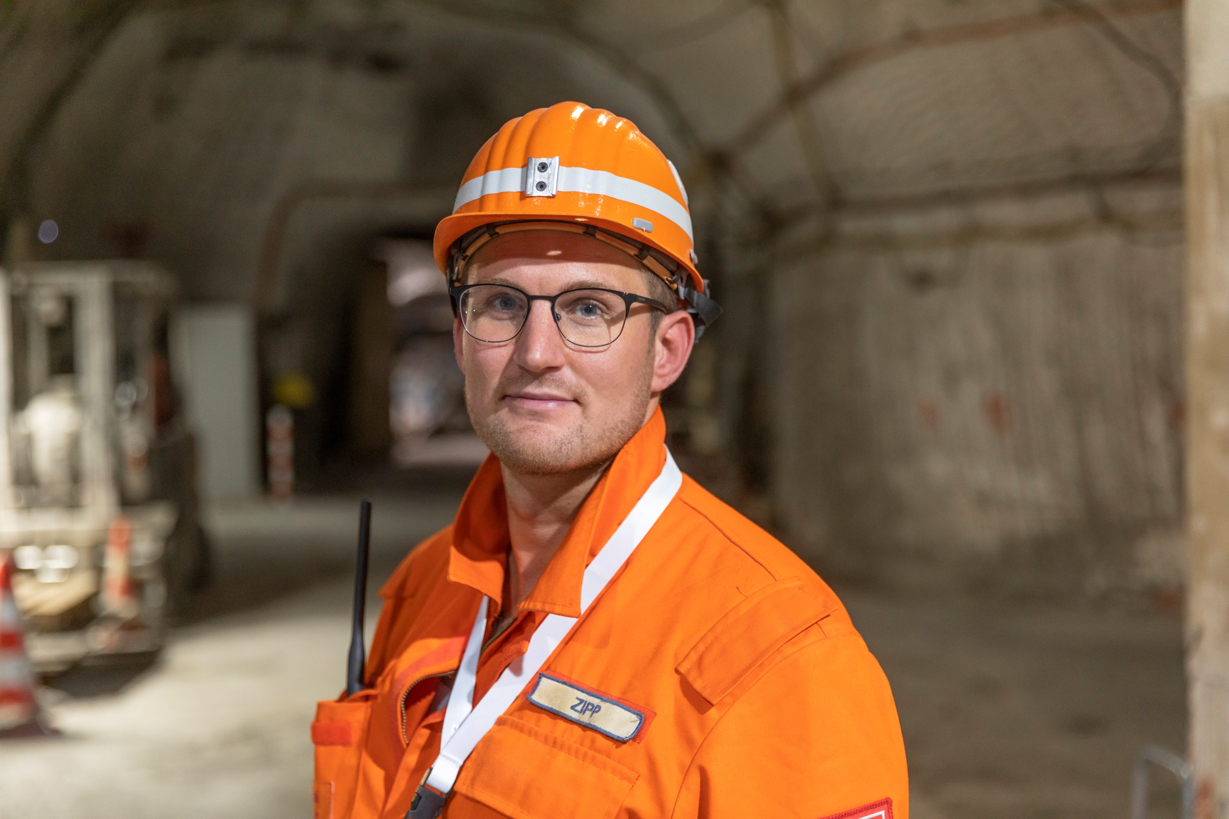 Ein Portrait von einem Mann mit orangenen Arbeitsanzug und Helm in einem Stollen