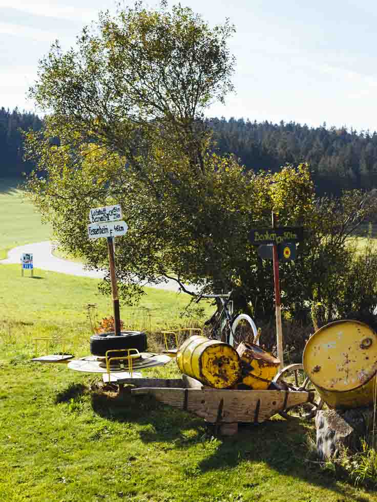 Auf einer Wiese stehen Schilder, daneben liegen gelbe Fässer