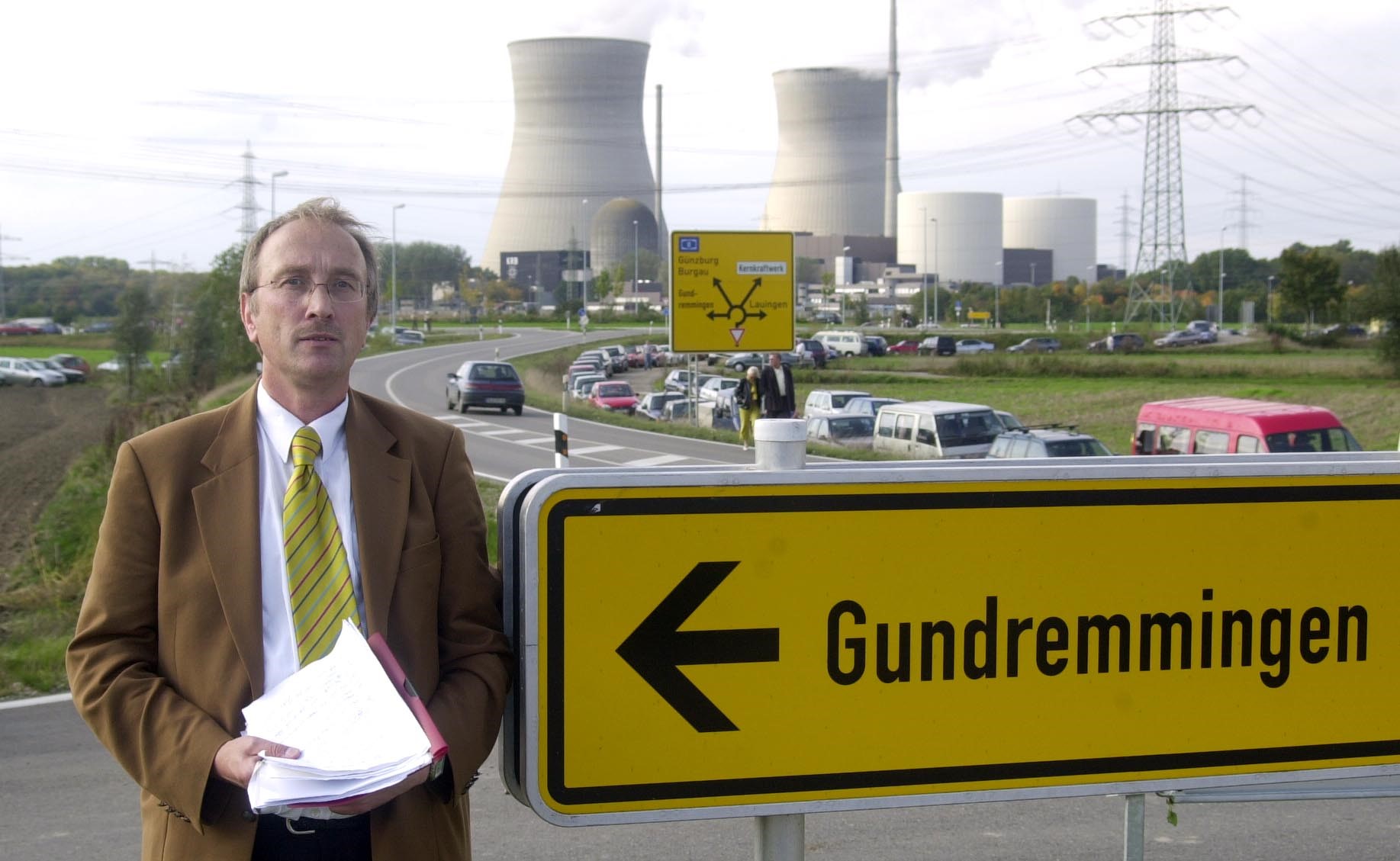 Ein  Mann steht vor Kühltürmen eines Atomkraftwerkes. Neben im steht das Ortsschild Grundremmngen