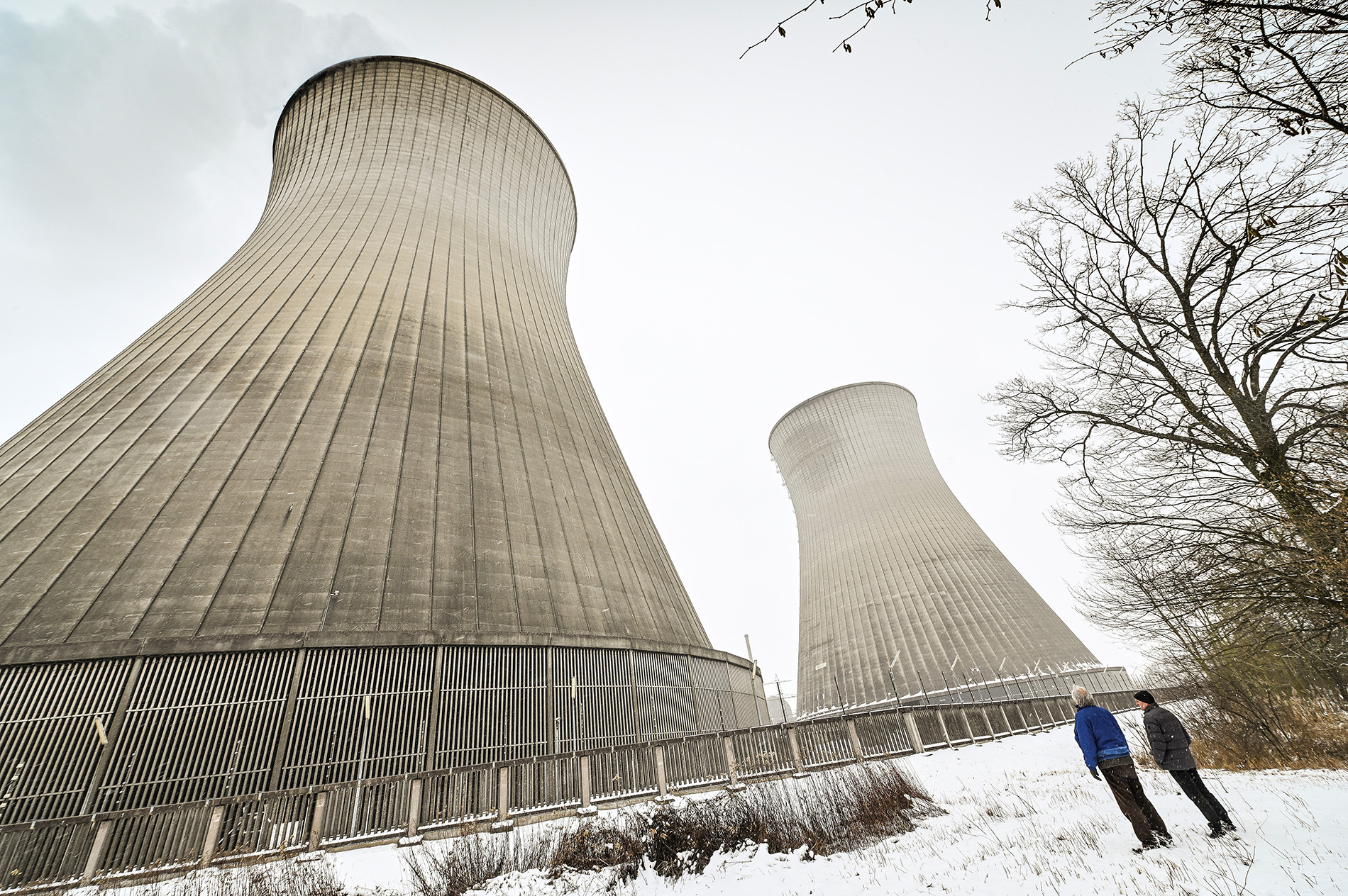 Zwei Männer stehen im Schnee vor den beiden Kühltürmen eines Atomkraftwerkes