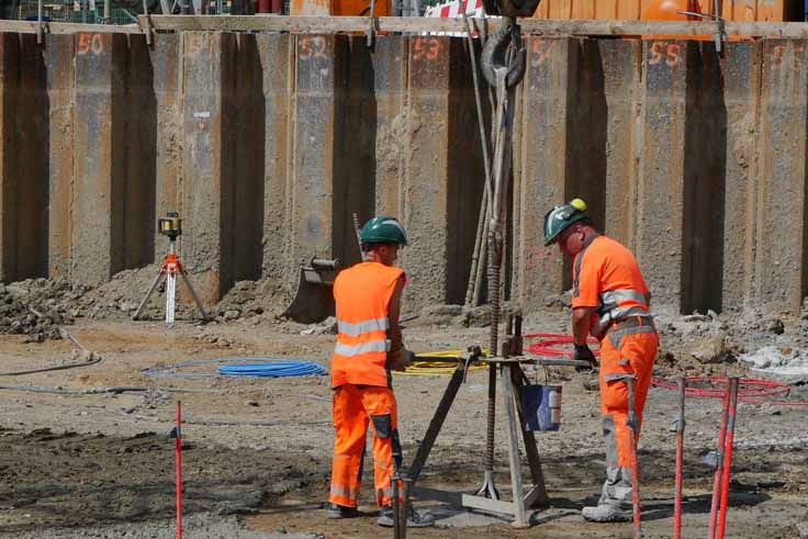 Zwei Personen mit orangefarbenen Warnwesten mit Gerät auf einer Baustelle