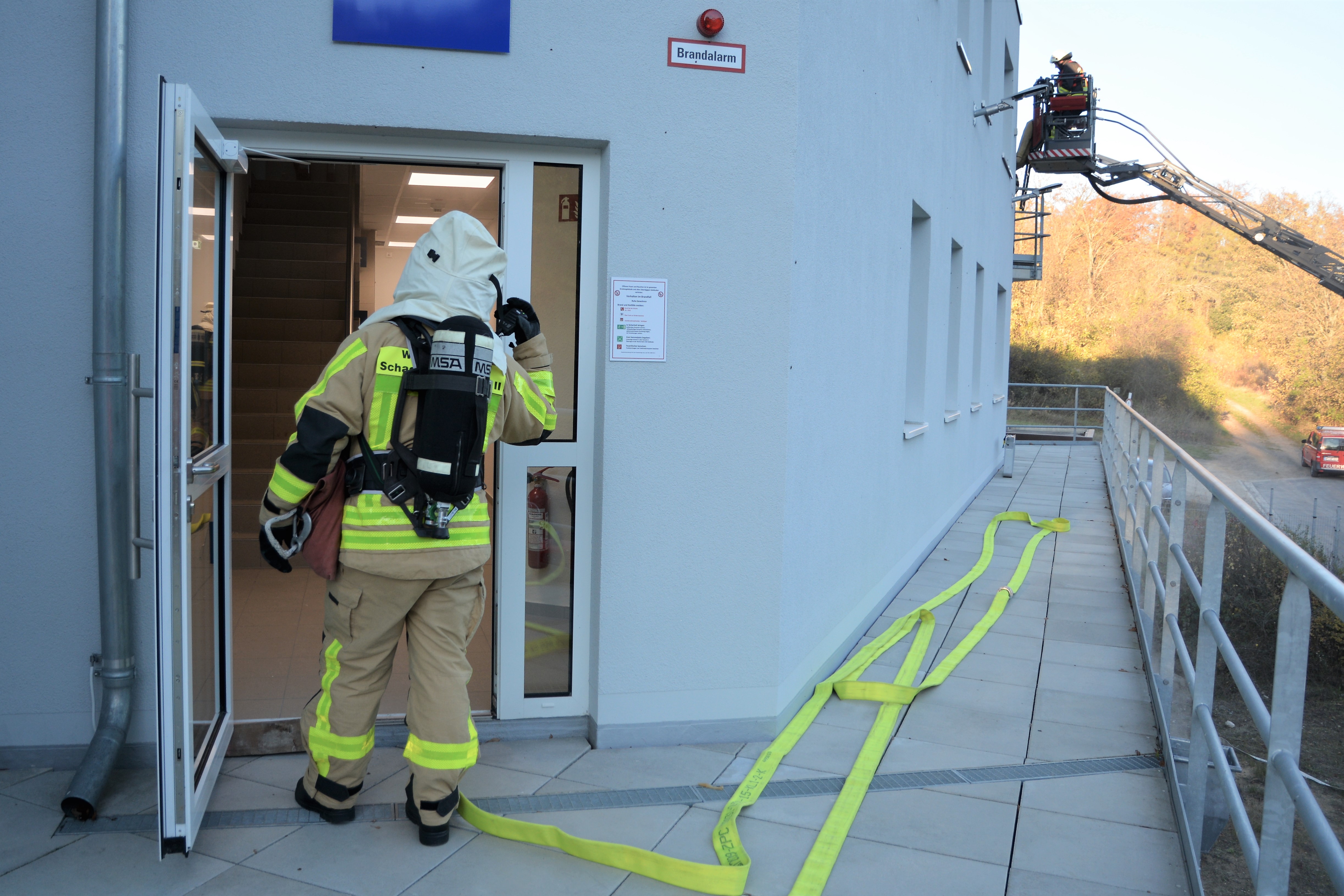 Ein Feuerwehrmann mit Atemschutz betritt ein Gebäude, an dessen Seite eine Drehleiter ausgefahren wird. 
