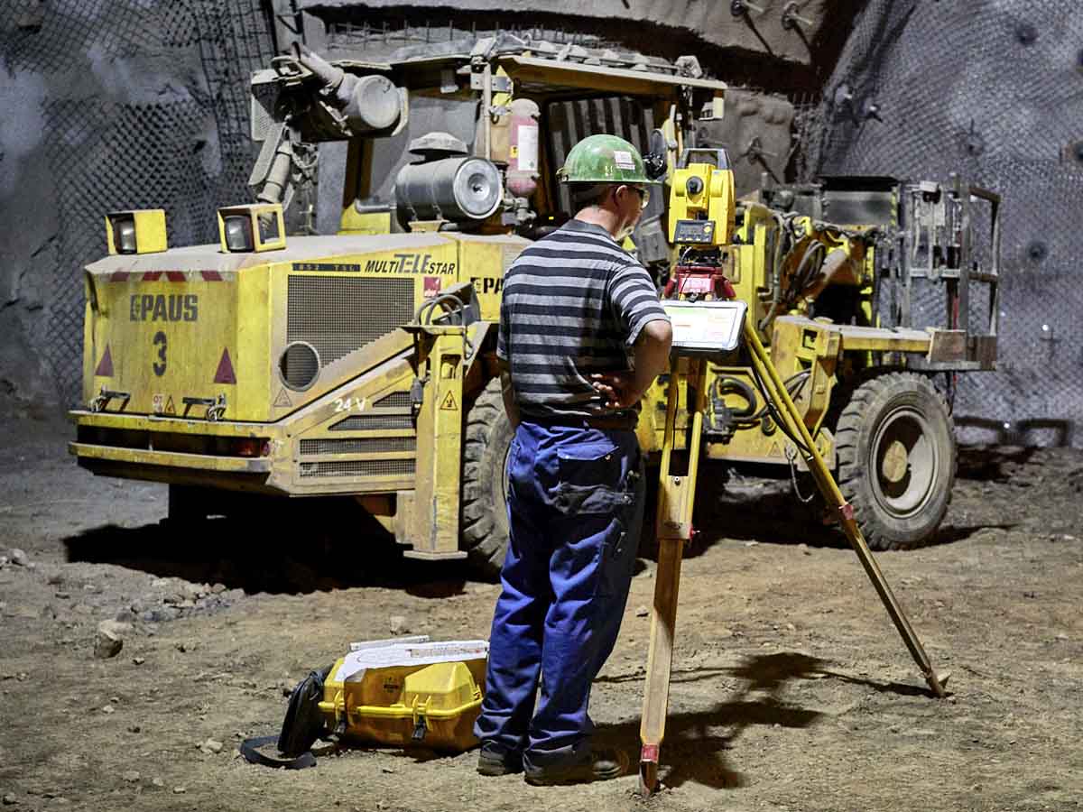 Arbeiter mit Vermessungsgerät unter Tage, im Hintergrund steht ein Baufahrzeug