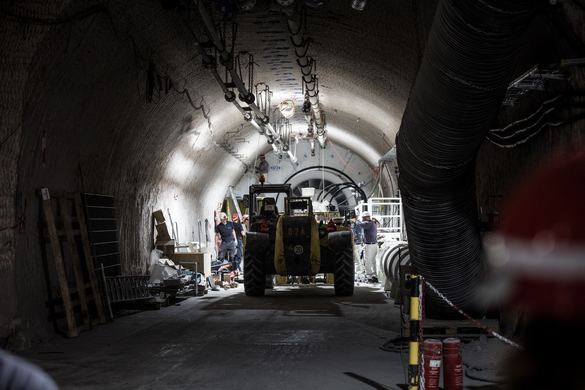 Blick in eine Strecke unter Tage. Das Foto zeigt die Rückansicht einer großen geparkten Baumaschine. Leuchtstoffröhren illuminieren das Fahrzeug.