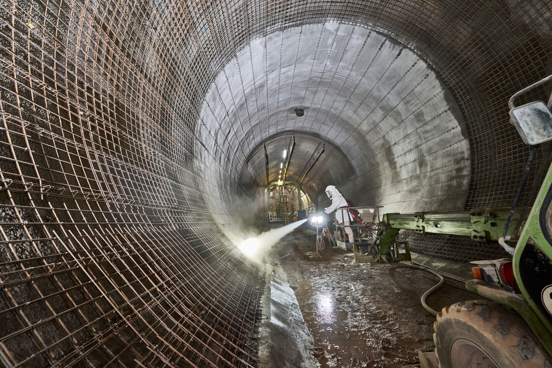 Ein in Schutzkleidung gehüllter Bergmann steht in einem unterirdischen Tunnel und spritzt Beton