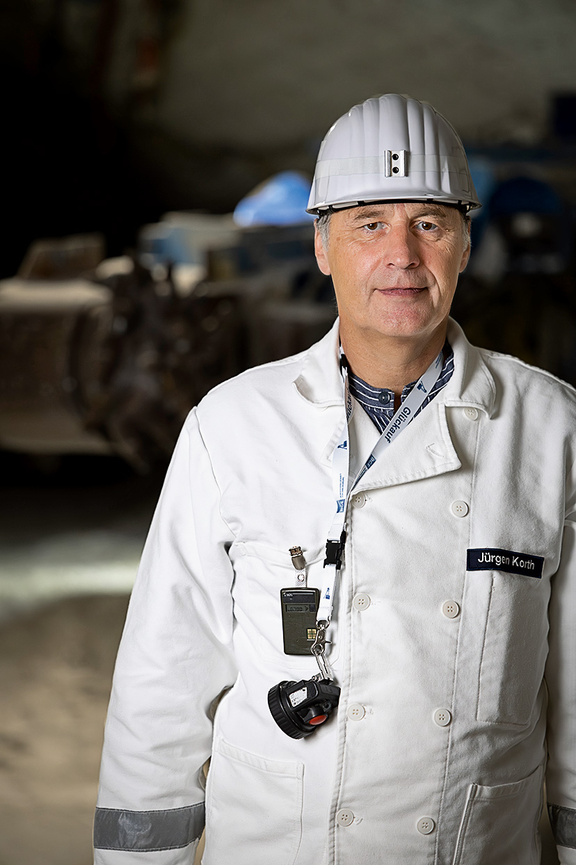 Ein Mann in weißer Bergmannskluft und mit weißem Schutzhelm lächelt in die Kamera.