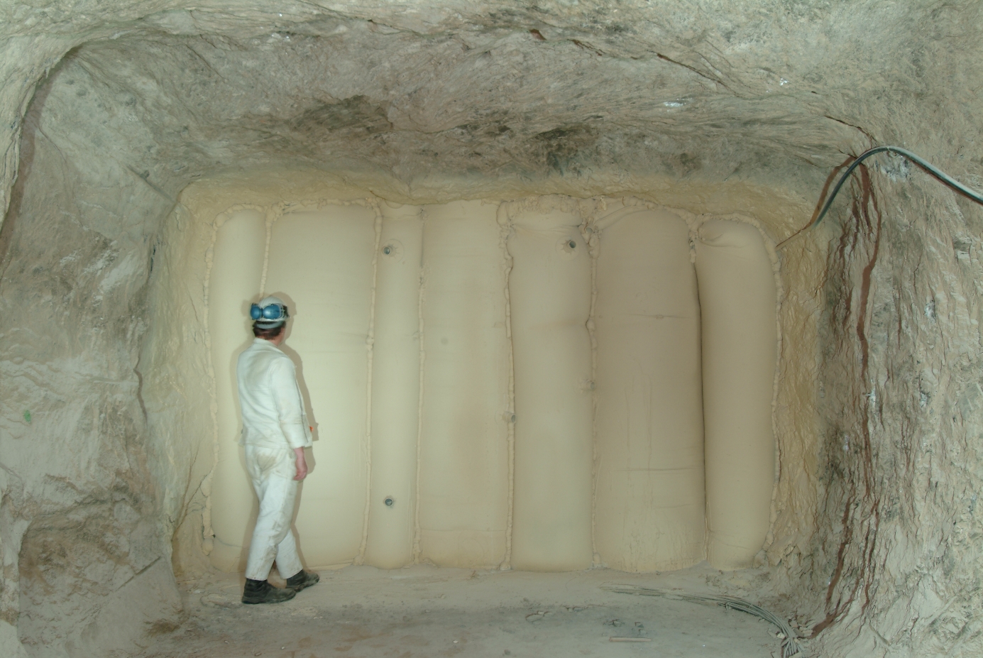 Eine Person in Sicherheitskleidung steht unter Tage vor einer Wand aus mit Beton gefüllten Stützschläuchen.